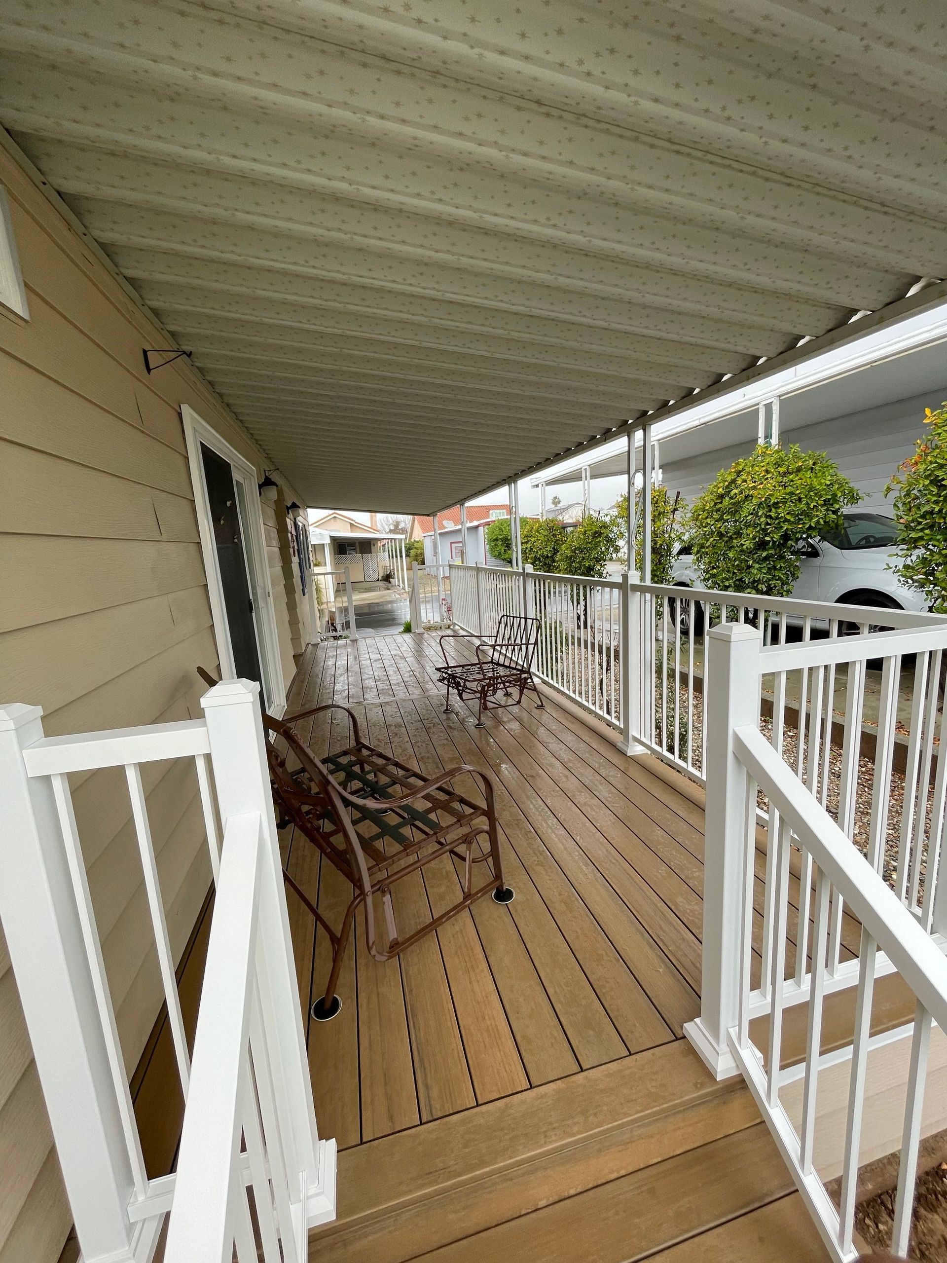 Covered wooden porch with metal patio furniture and white railings beside a house