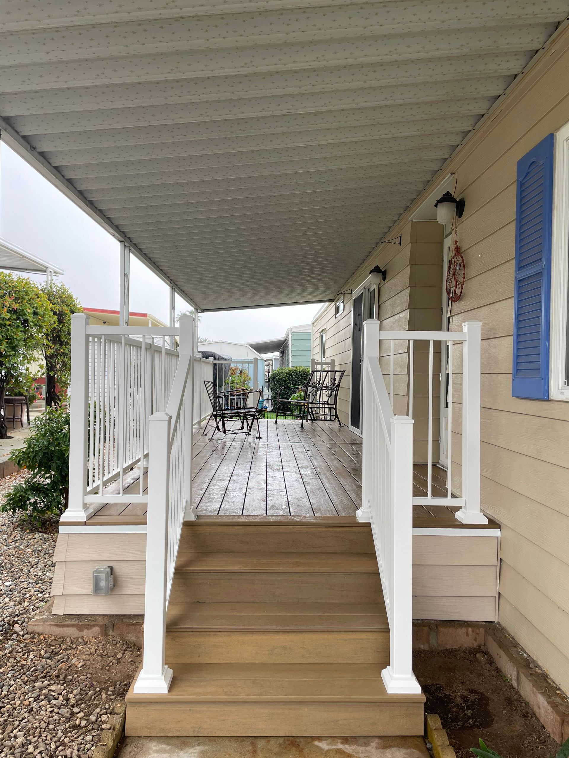 Covered porch with wooden steps, white railings, and blue shutters on a house.