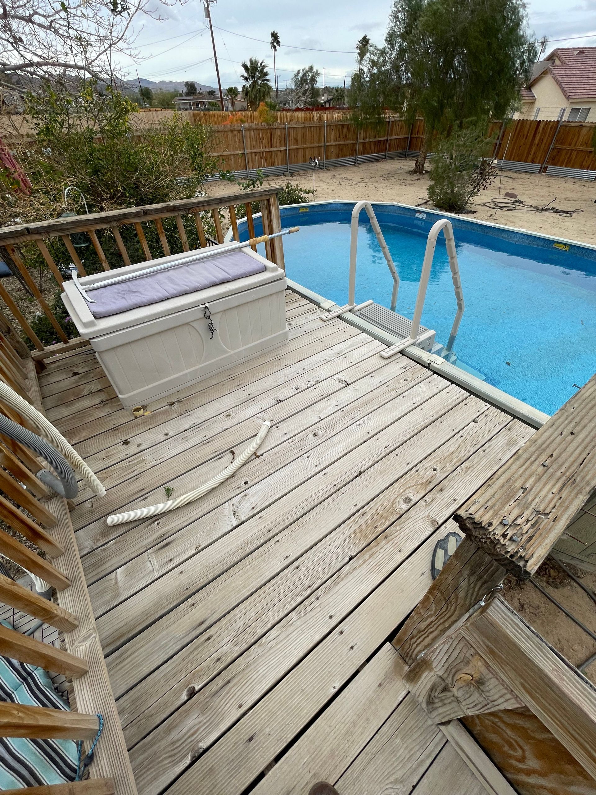Wooden deck with white bench beside a blue backyard pool and metal handrails.