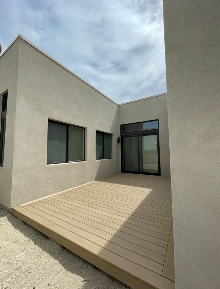 Exterior view of a beige stucco building with a wooden deck and sliding glass doors.