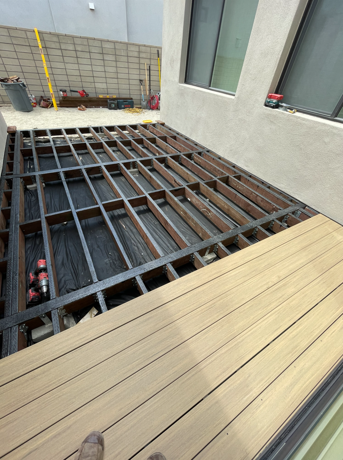 Deck construction: framing visible, composite decking partially installed, tools in background.