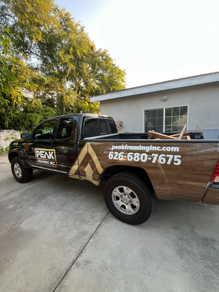 Black pickup truck with wood grain design, parked outdoors; business name and phone number on the side.