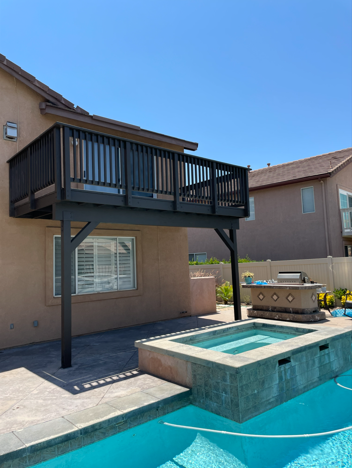 Black deck on a house overlooking a pool and spa on a sunny day.