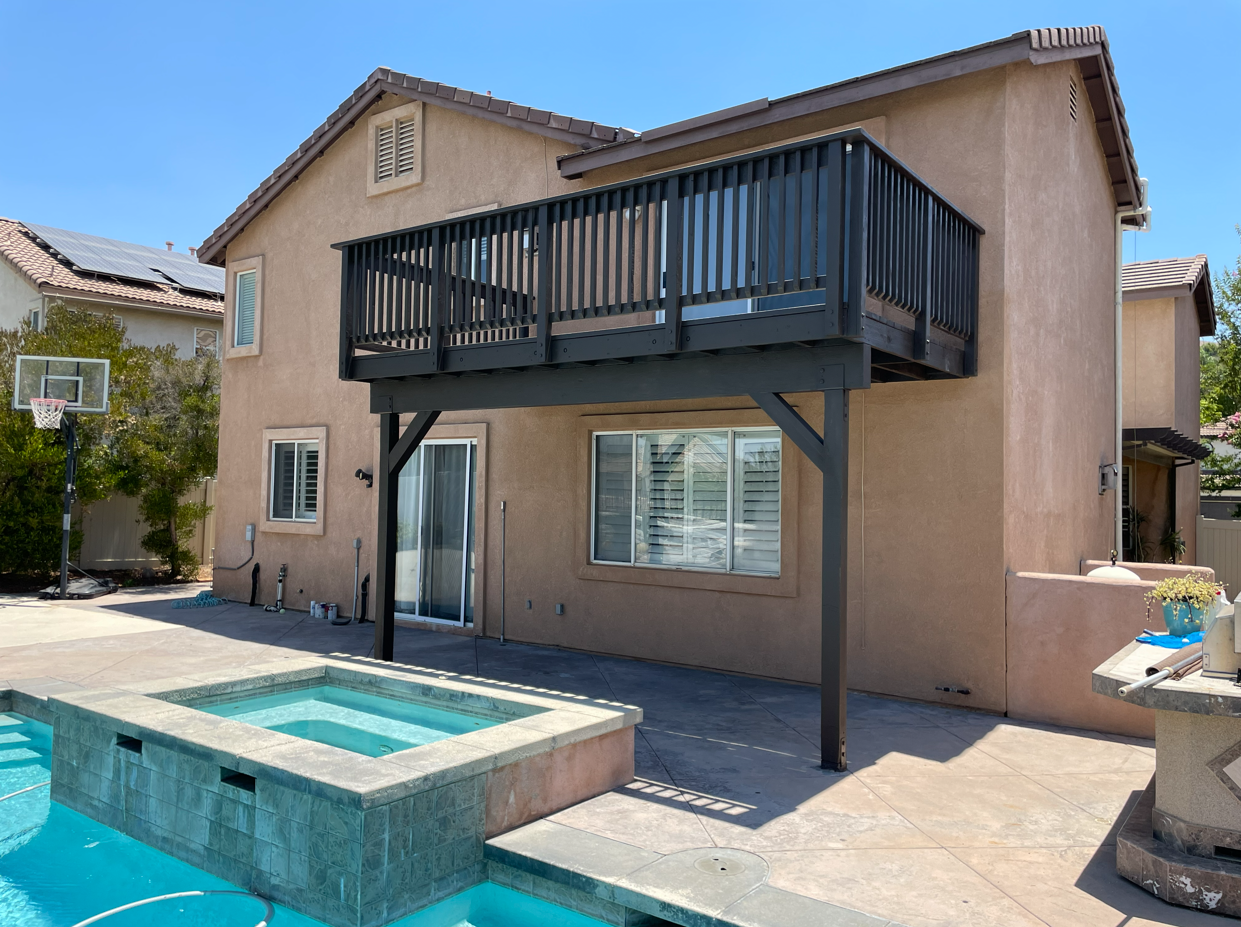 Two-story house with a dark wooden deck over a pool and jacuzzi.