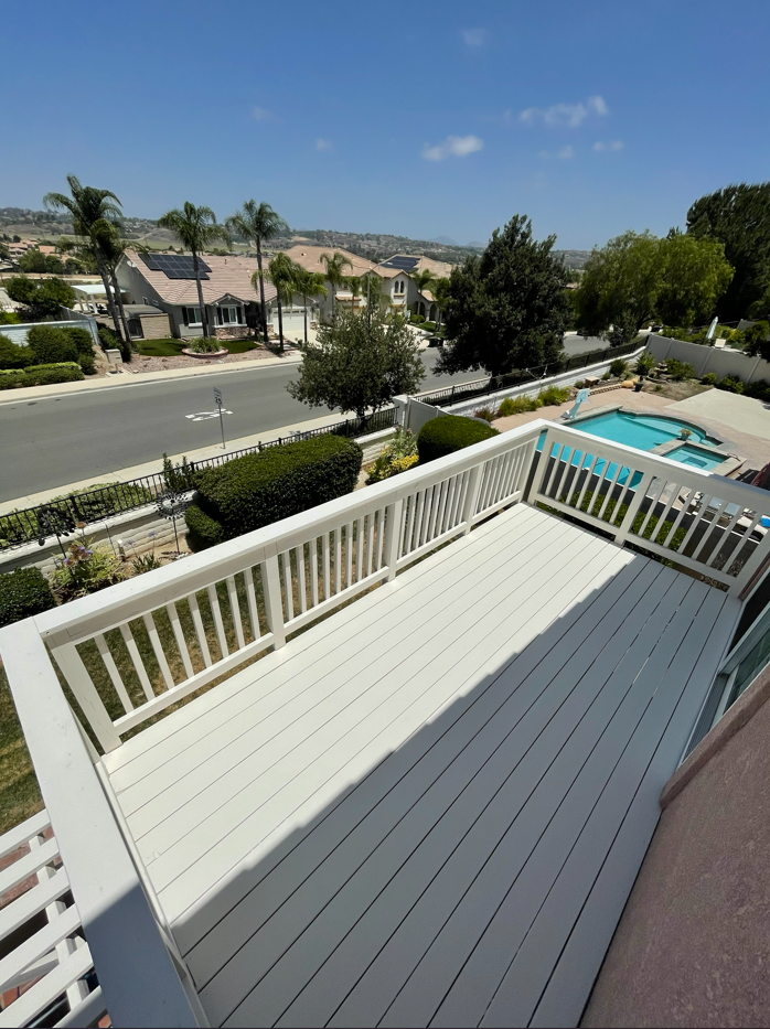 White painted deck with railing overlooking a street, homes, and a pool on a sunny day.