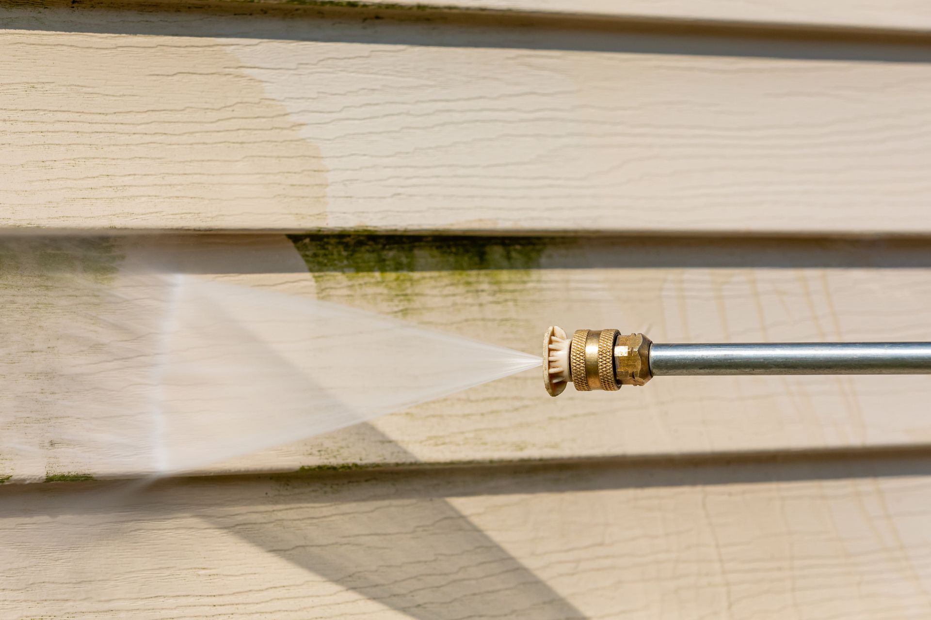 A person is using a high pressure washer to clean a house 's siding.