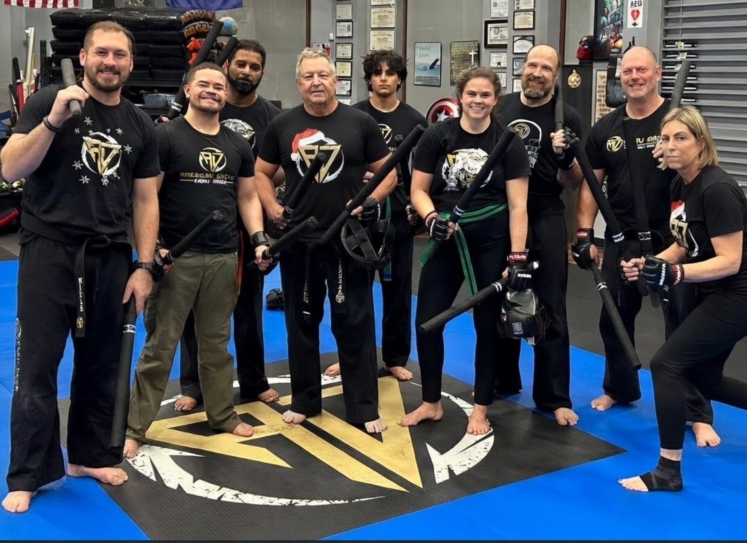 Group of children in martial arts attire posing, some with arms around each other, in a gym.