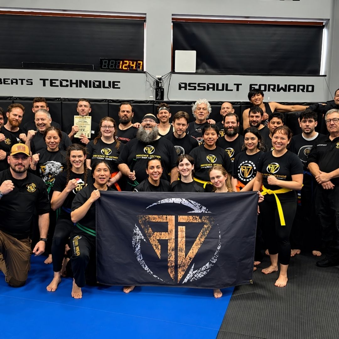 Five people in jiu-jitsu gear pose together in a gym. Smiling, some have arms around each other. Machado logo visible.