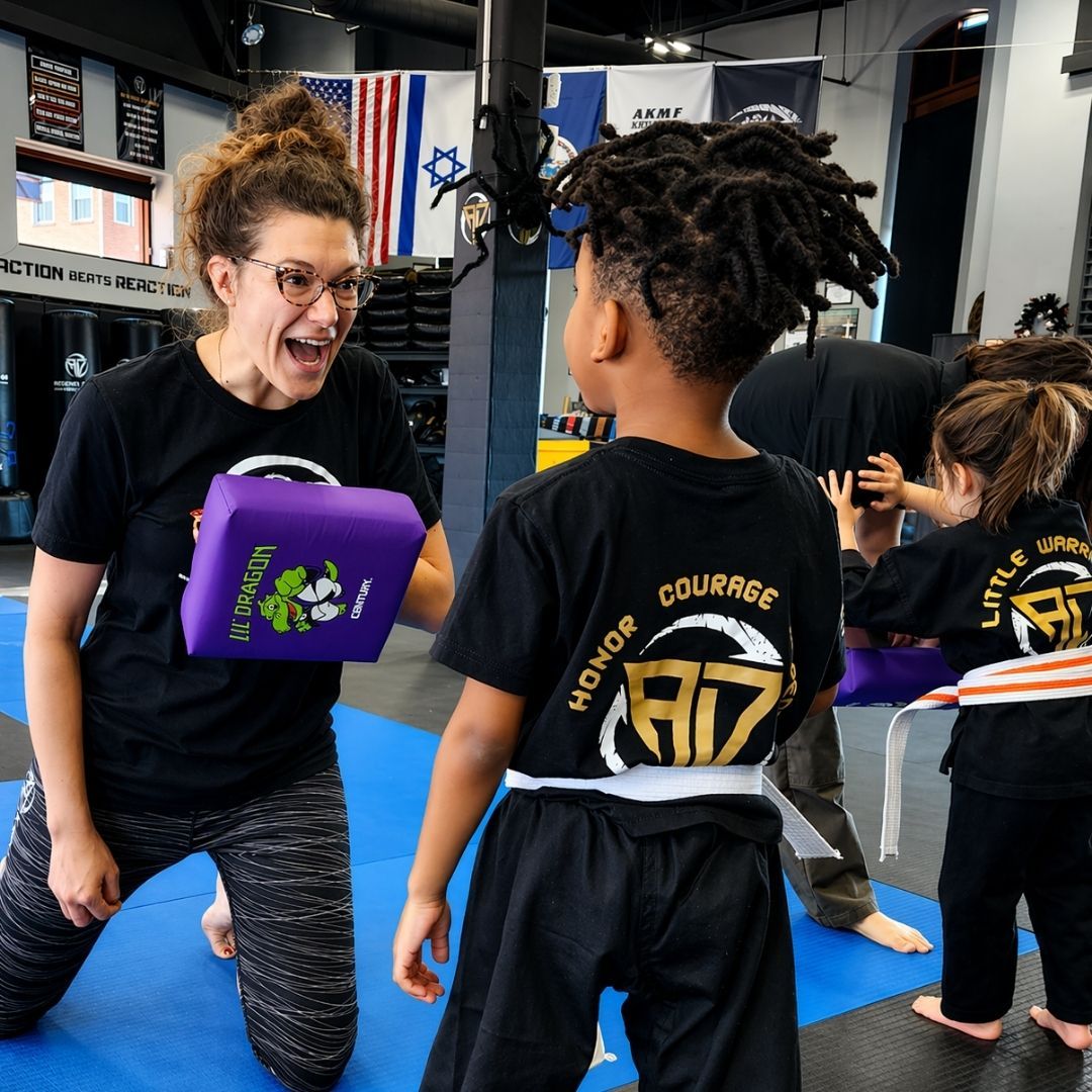Two children in black and white martial arts uniforms practice a chokehold on a mat. One child smiles.