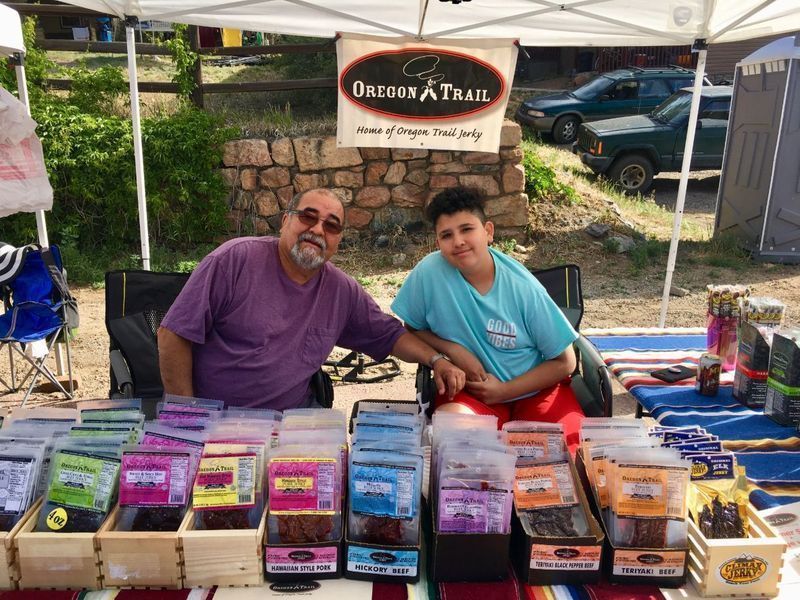 Two people smiling at a market stand selling jerky. 