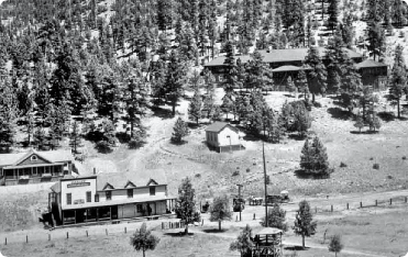 Historic black and white photo of a hillside town with multiple buildings nestled among trees.