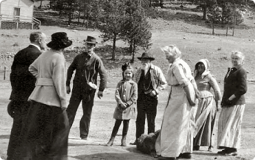 Group of people standing outdoors, some wearing hats. A child in a coat stands in the center.