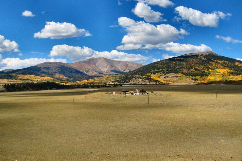 Mountains rise above a grassy plain under a blue sky with fluffy white clouds.