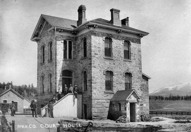 Old stone courthouse with people standing on steps, mountains in the background.