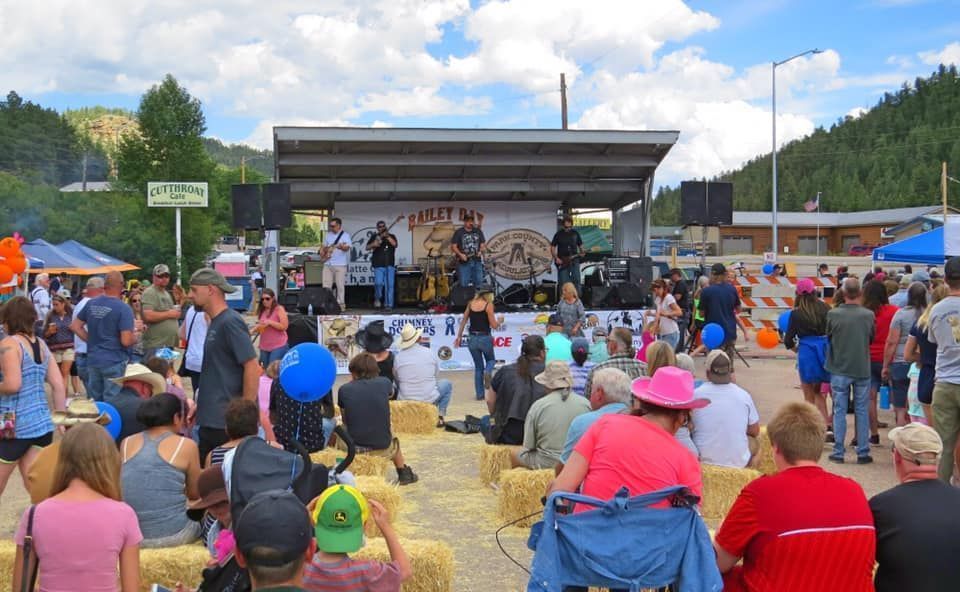 A band performs on an outdoor stage at a festival, with a crowd seated on hay bales.