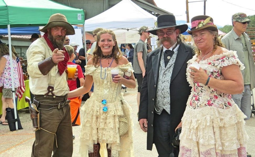 Four people in Wild West attire at an outdoor event, smiling and posing.