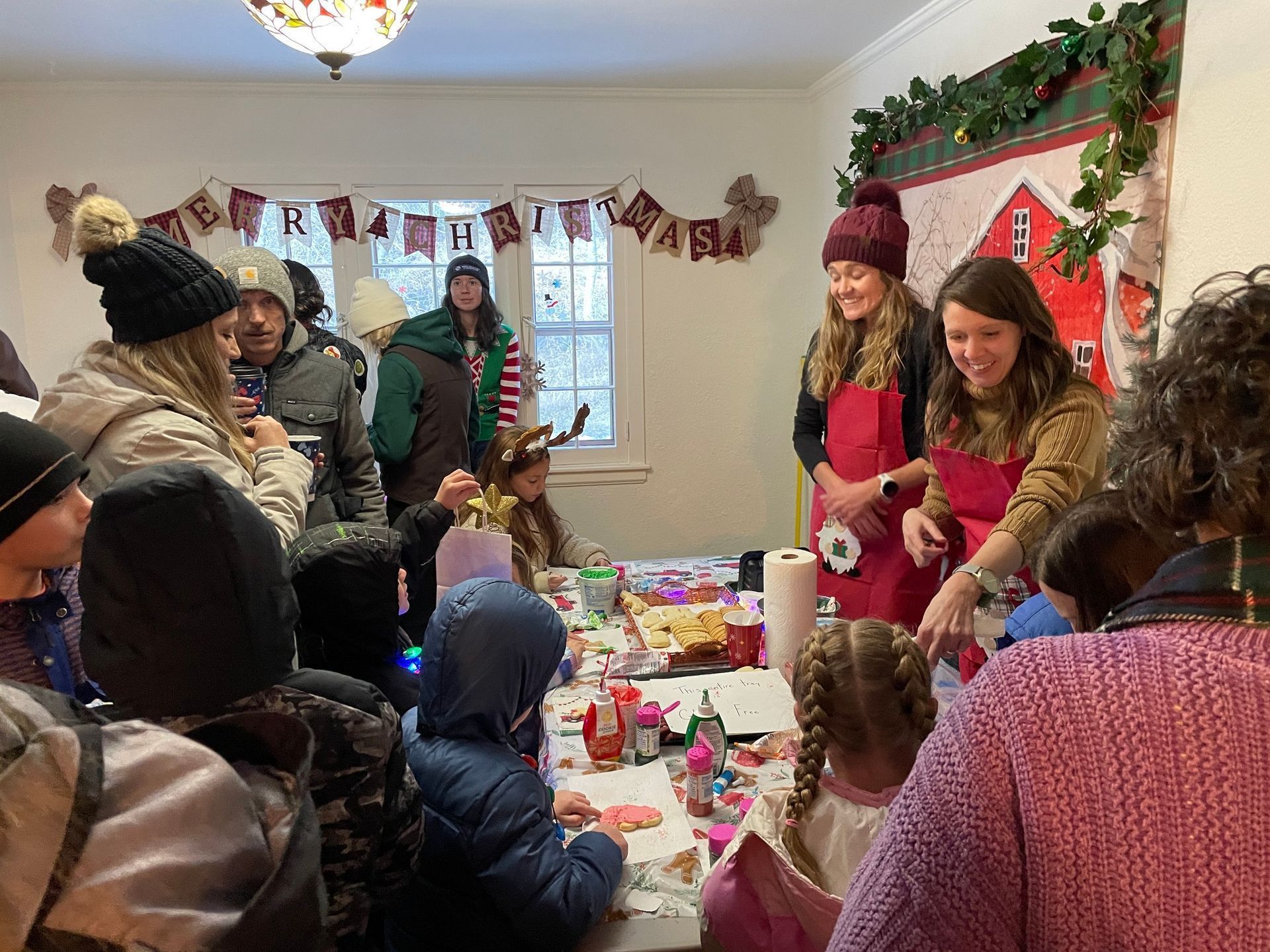 People decorating cookies at a holiday event, festive decorations, smiling, indoor.