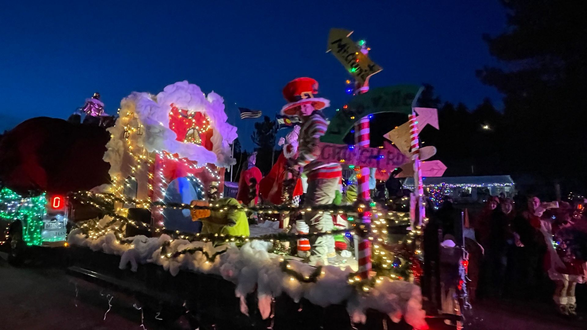 Illuminated holiday parade float with figures, candy canes, and signs at night.