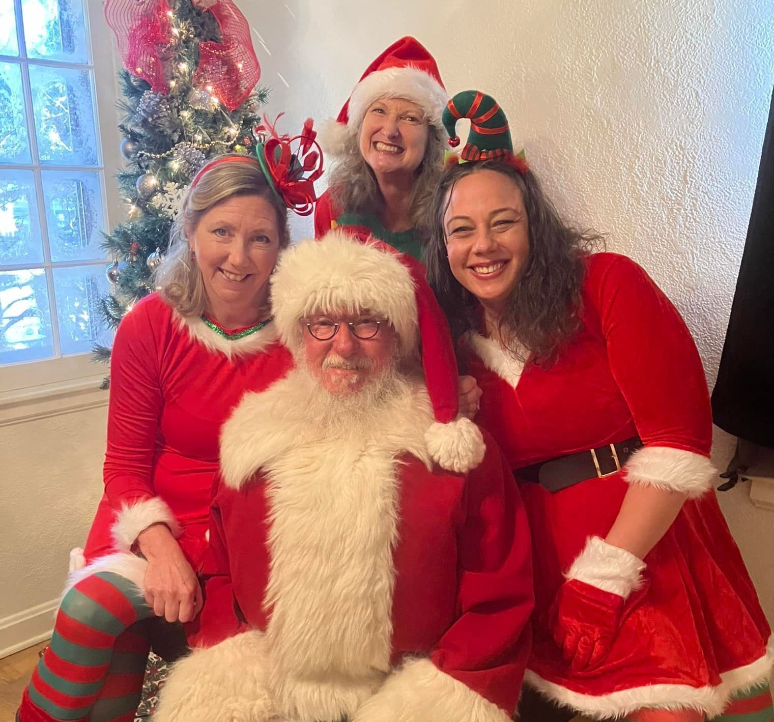 Santa poses with three women in festive holiday attire.