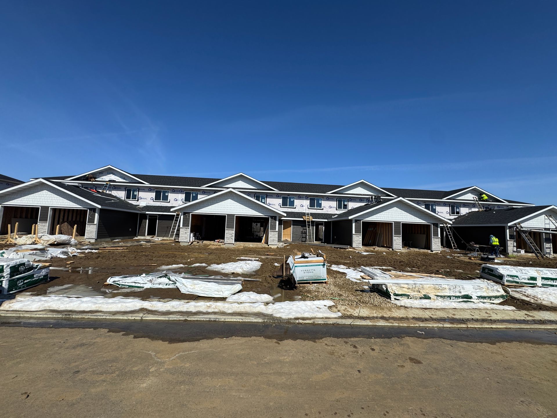 Row of new houses under construction with snow patches and a clear blue sky