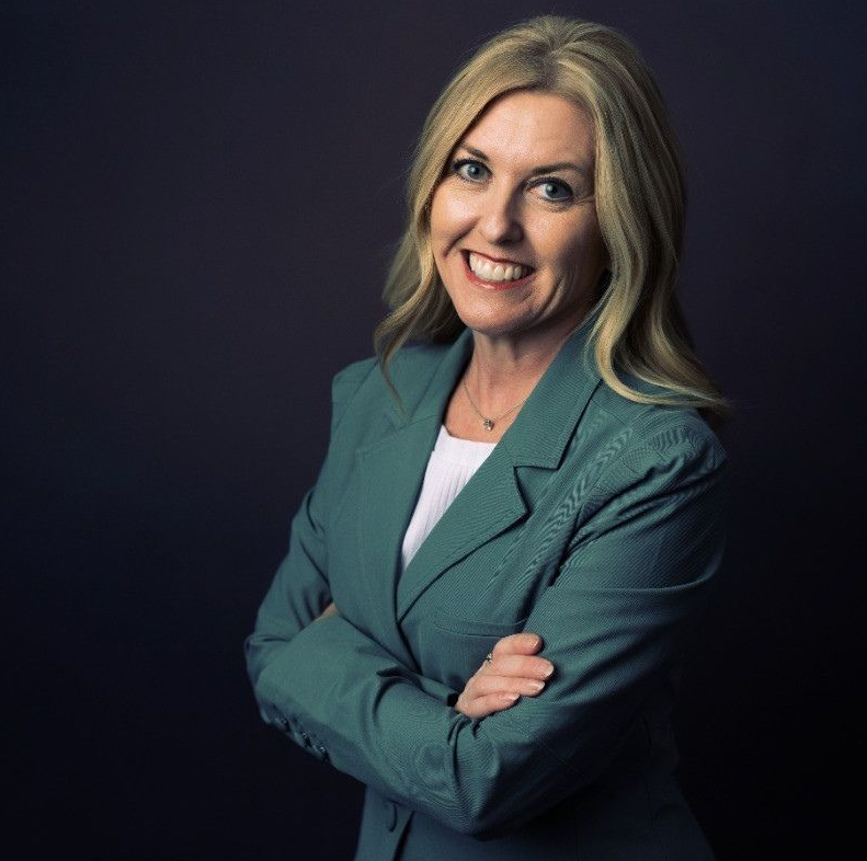 Portrait of a smiling woman in a teal blazer with arms crossed on a dark background