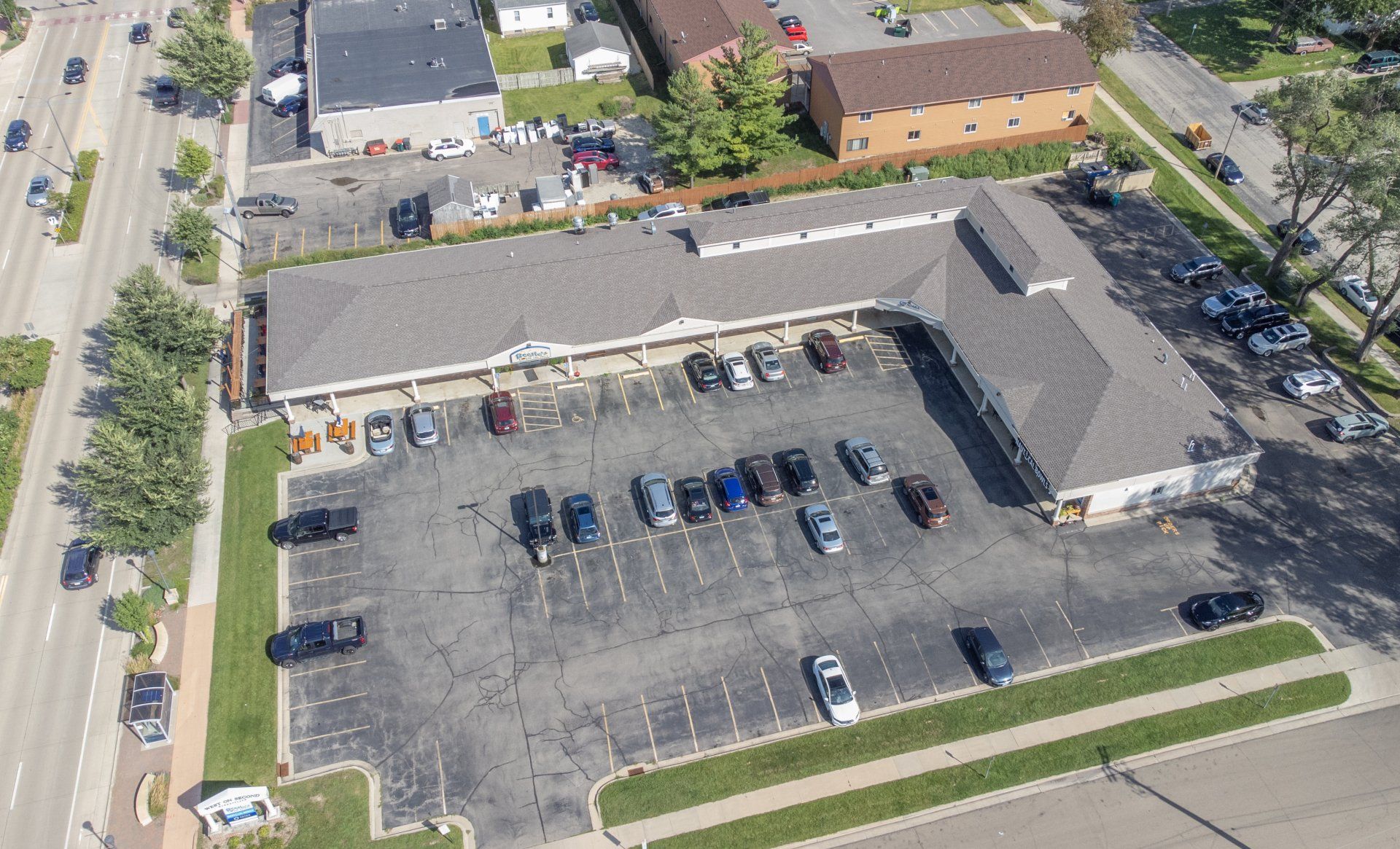 Aerial view of a large commercial building with a parking lot and several parked cars.