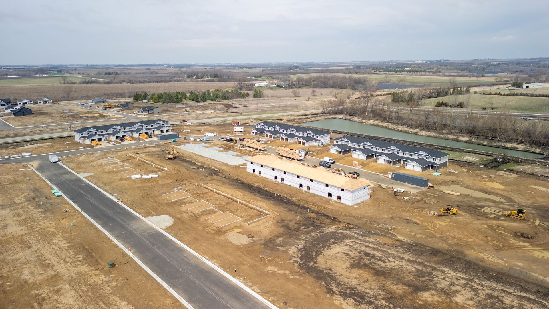 Aerial view of a construction site with row homes, roads, and open land surrounding the development