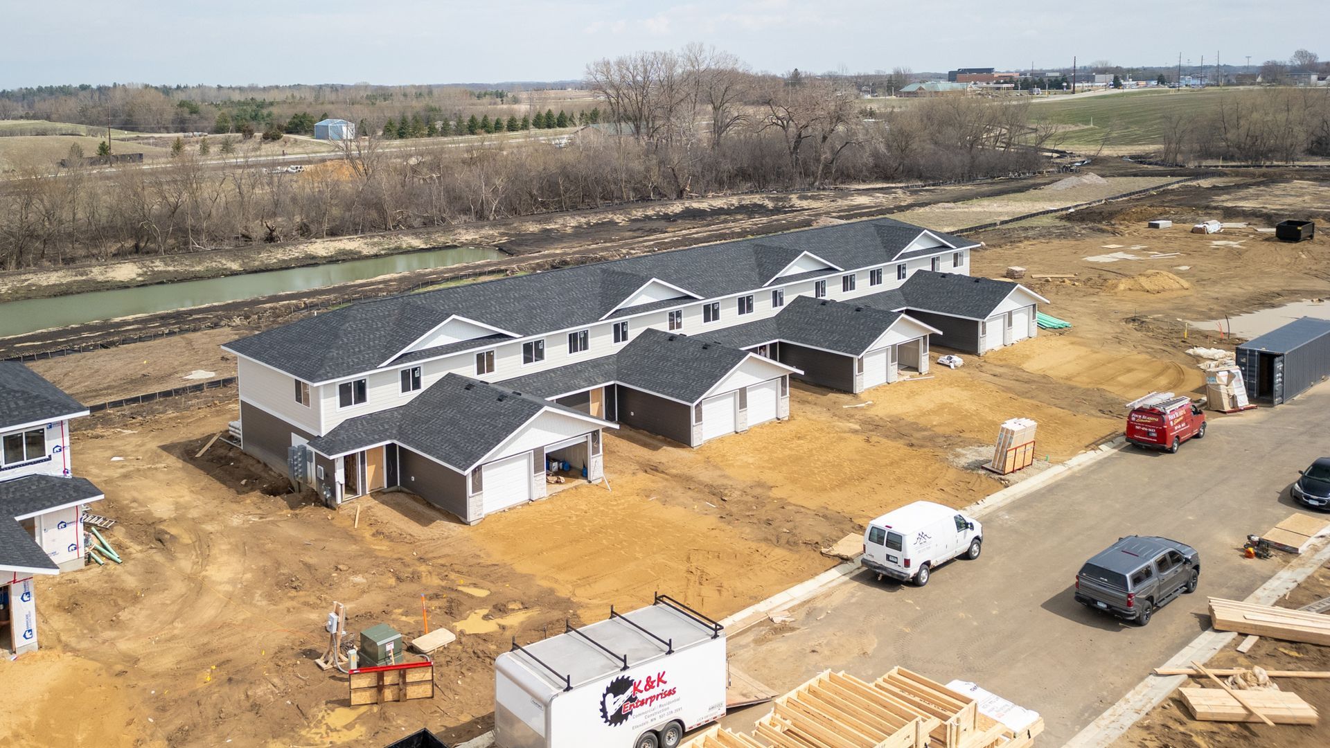 Aerial view of a new apartment complex under construction with trucks, white vans, and dirt lot.