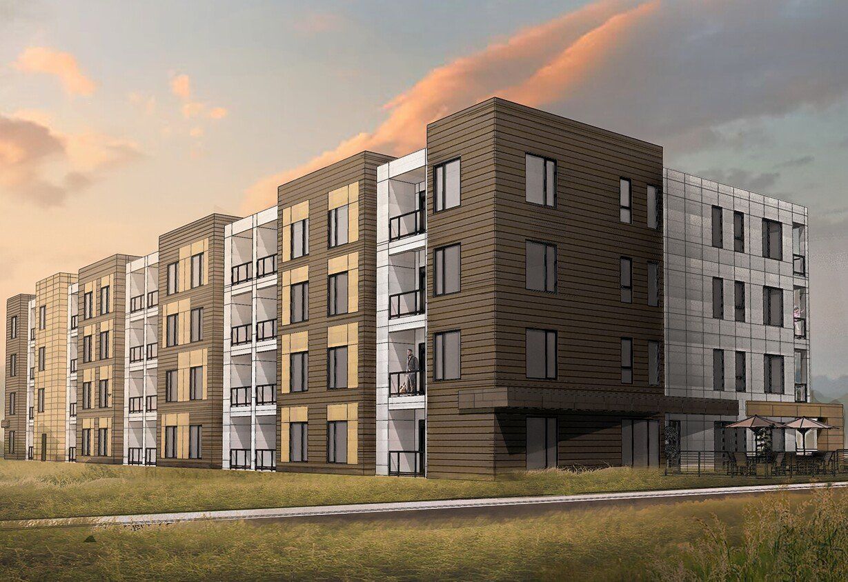 Modern apartment buildings with brown and white facades beside a grassy field at sunset