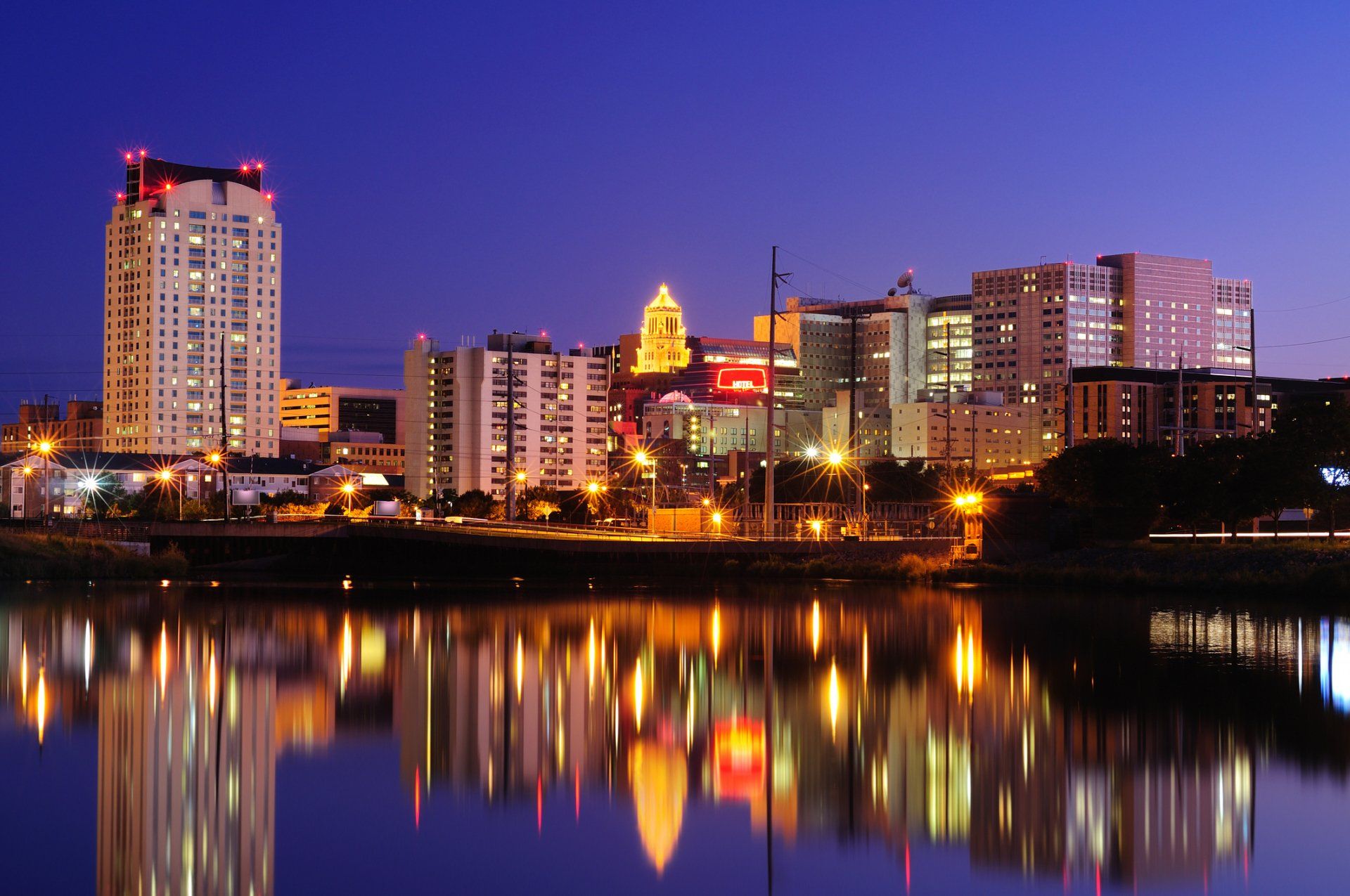 City skyline at dusk with colorful building lights reflected on calm water