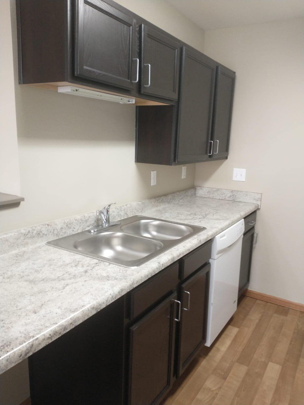 Kitchen with dark brown cabinets, light countertops, stainless steel sink, and white appliances.