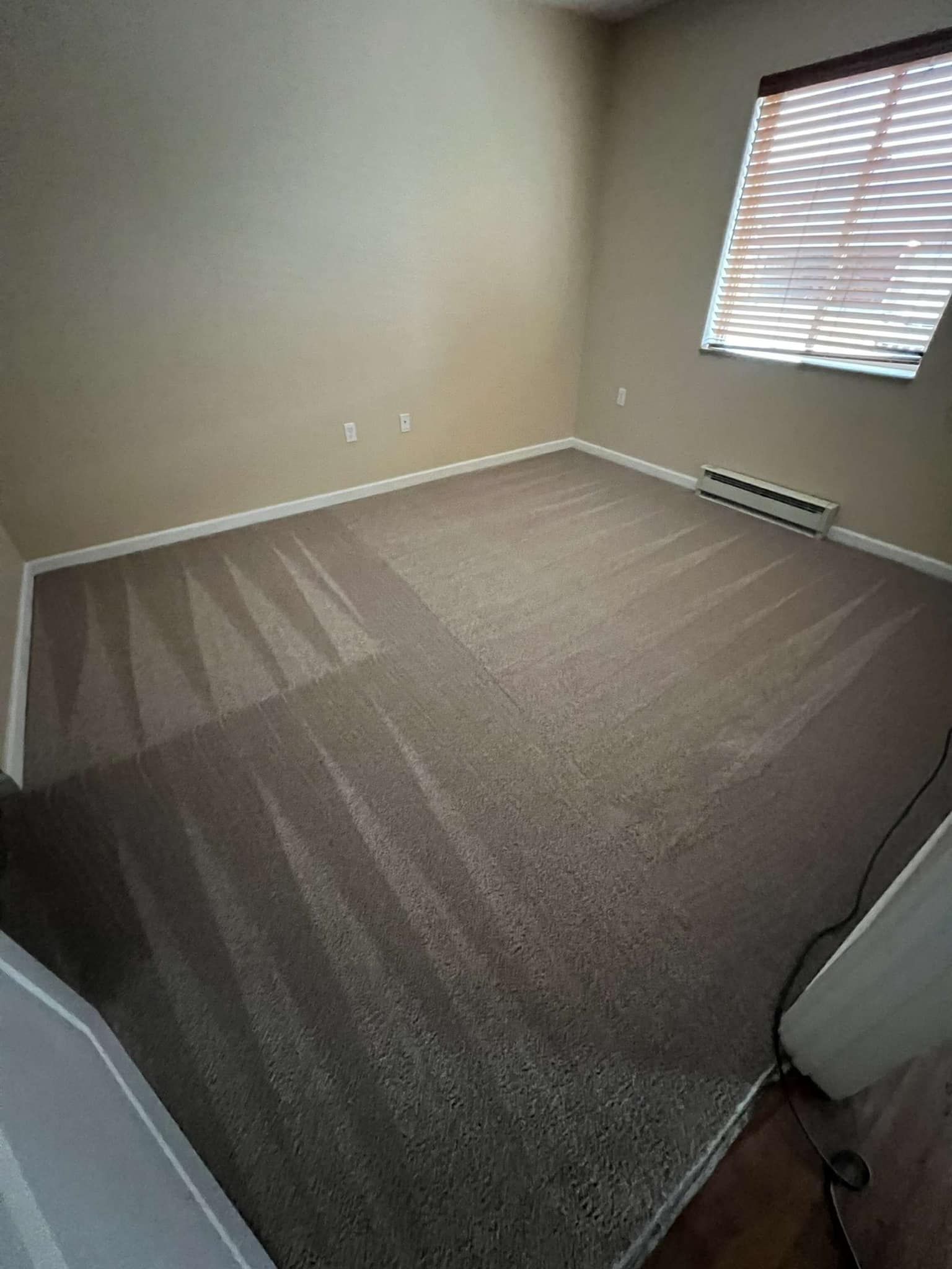 Empty room with beige walls, brown carpet, and a window with blinds.