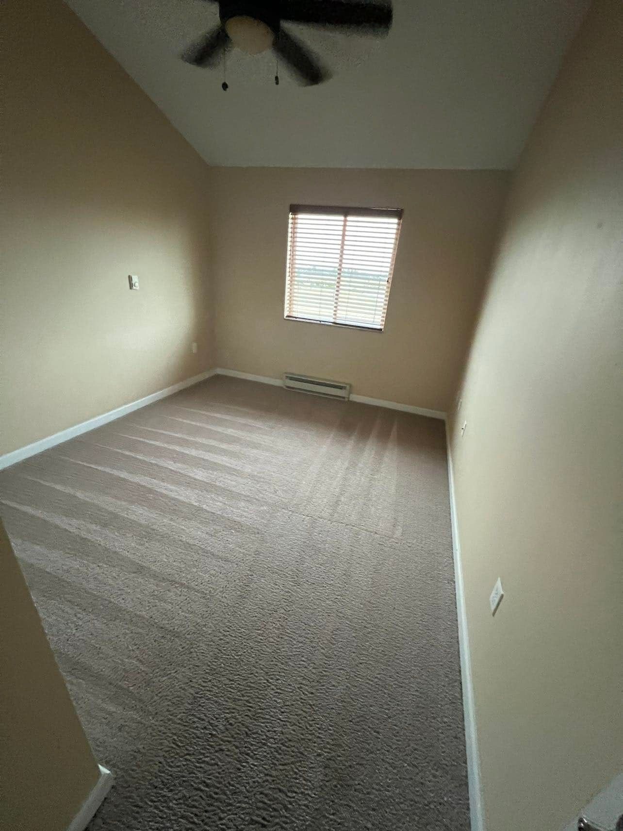 Empty room with beige walls, brown carpet, window with blinds, and ceiling fan.