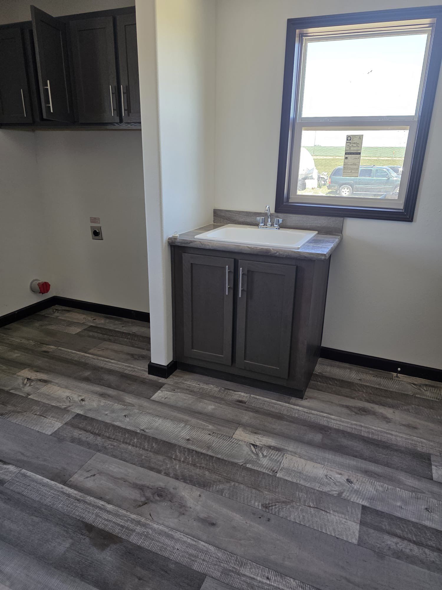 A laundry room with gray cabinets, sink, and window. Gray and brown wood-look flooring.