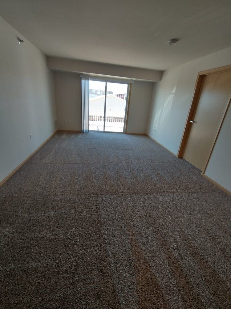 Empty room with brown carpet, sliding glass door, and a door on the right.