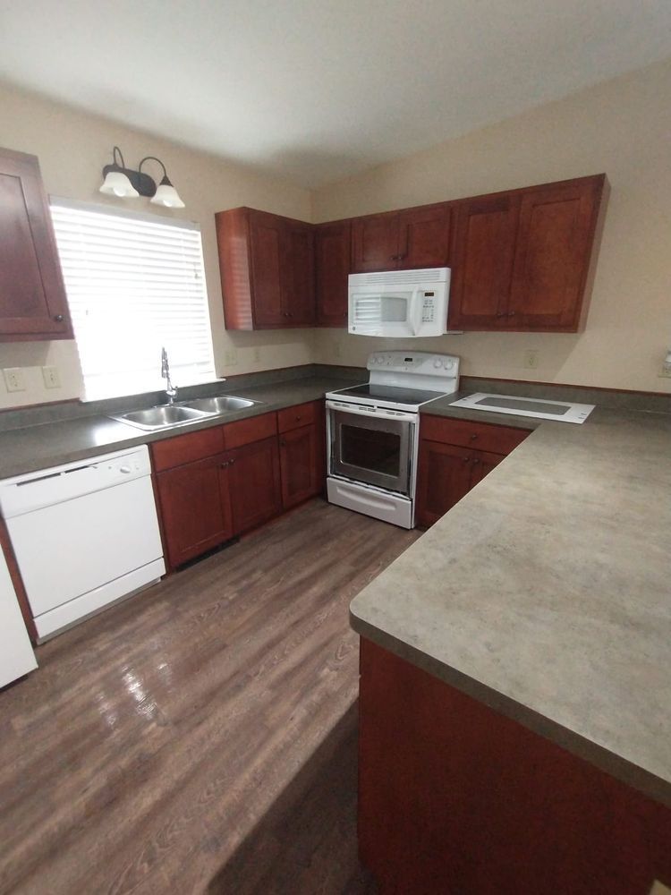 Kitchen with dark wood cabinets, white appliances, and gray countertops.