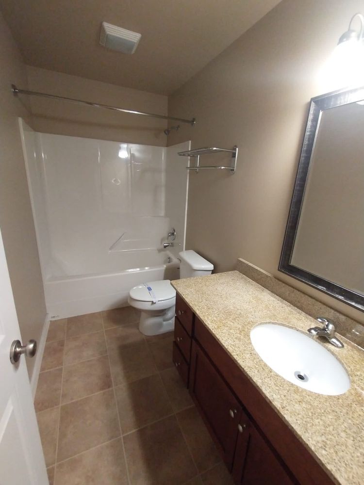 Bathroom with beige walls, brown tile, white tub, toilet, sink, and dark wood vanity.