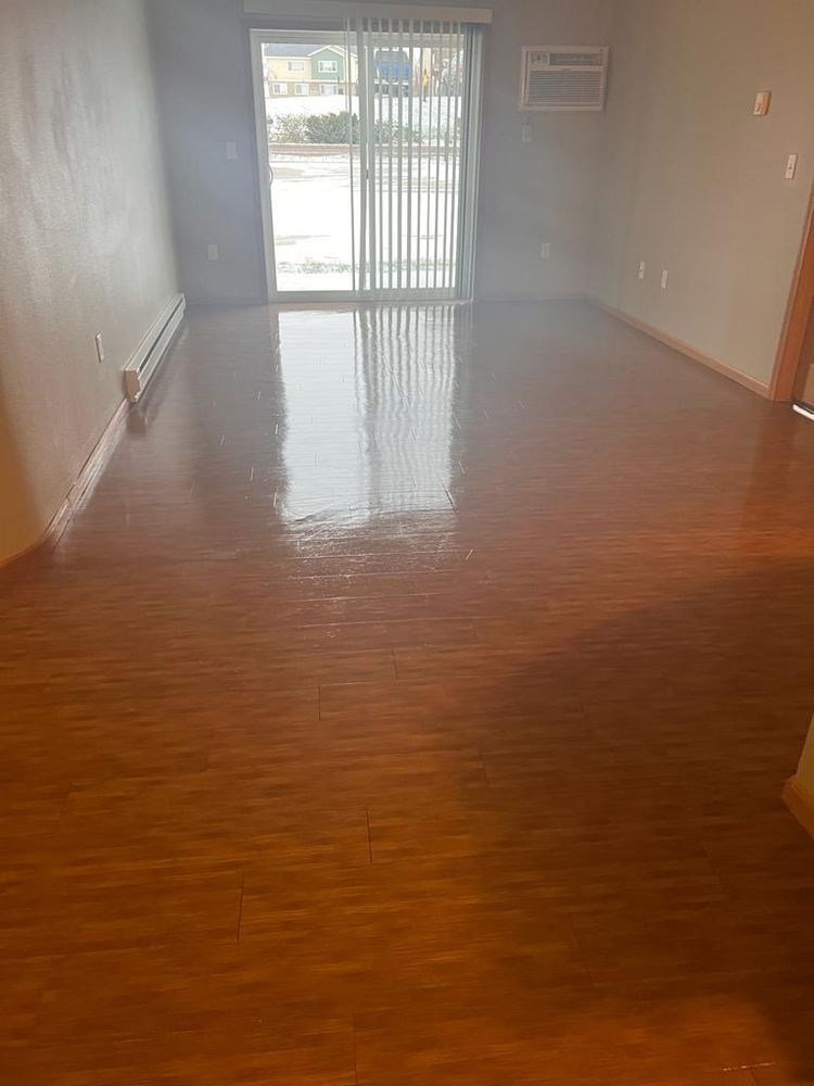 Empty room with glossy wood-look flooring and sliding glass door, a wall-mounted AC unit, and radiator.