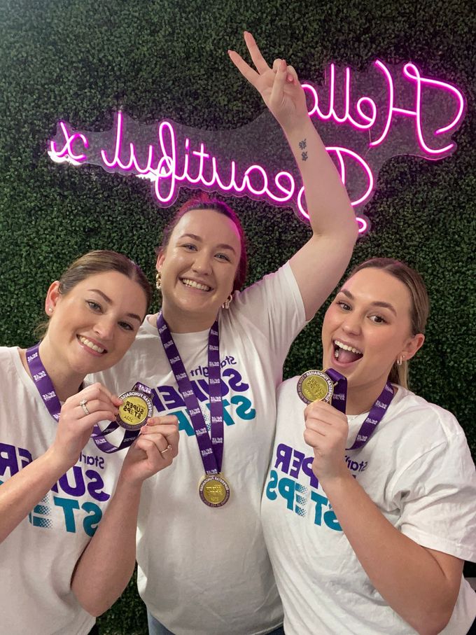 Three women are holding medals in front of a neon sign. — Bloom Skin Brows & Beauty In Bungalow, QLD