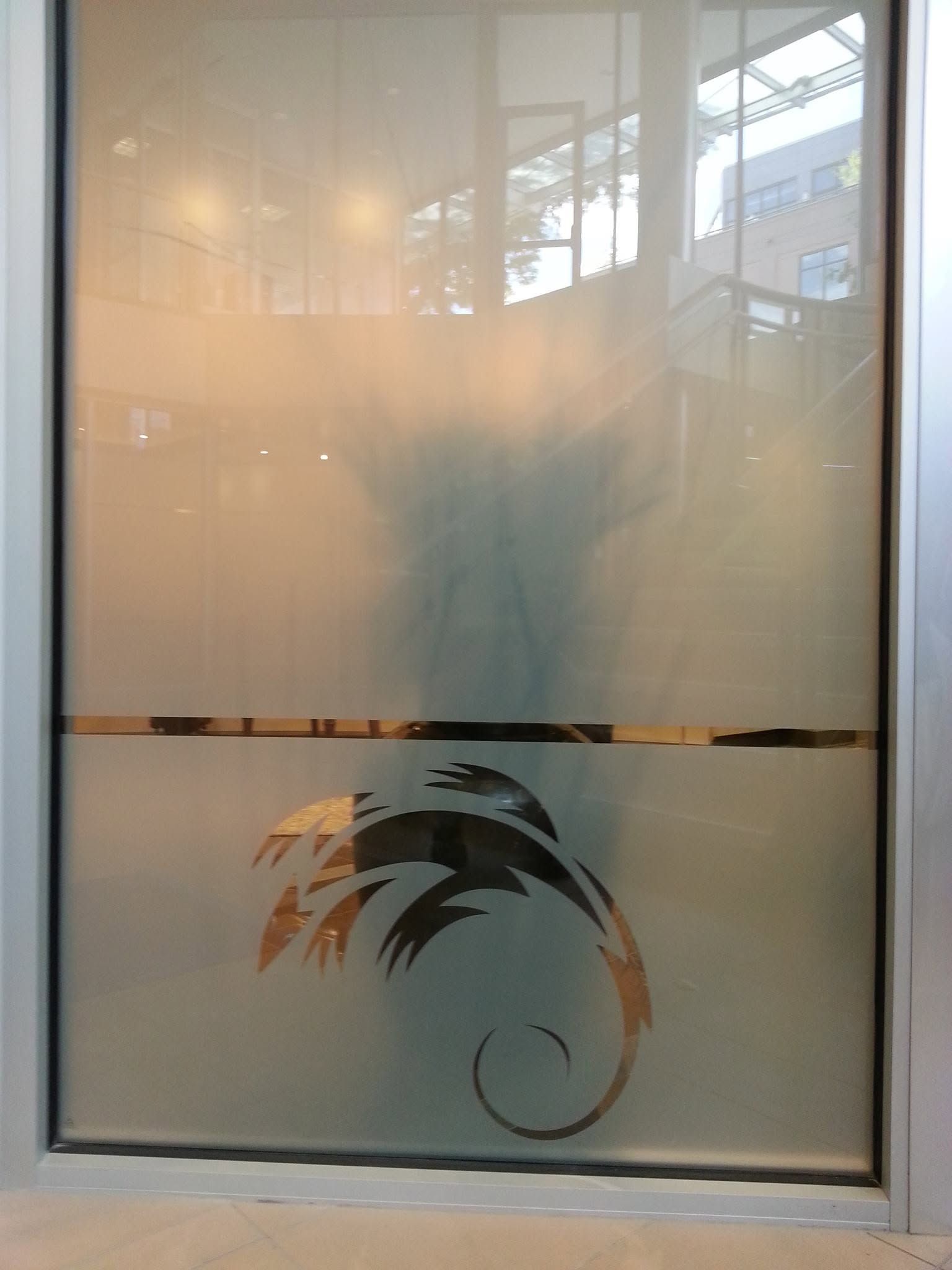 Frosted glass door with a black decorative palm tree and a horizontal stripe, reflecting a building outside