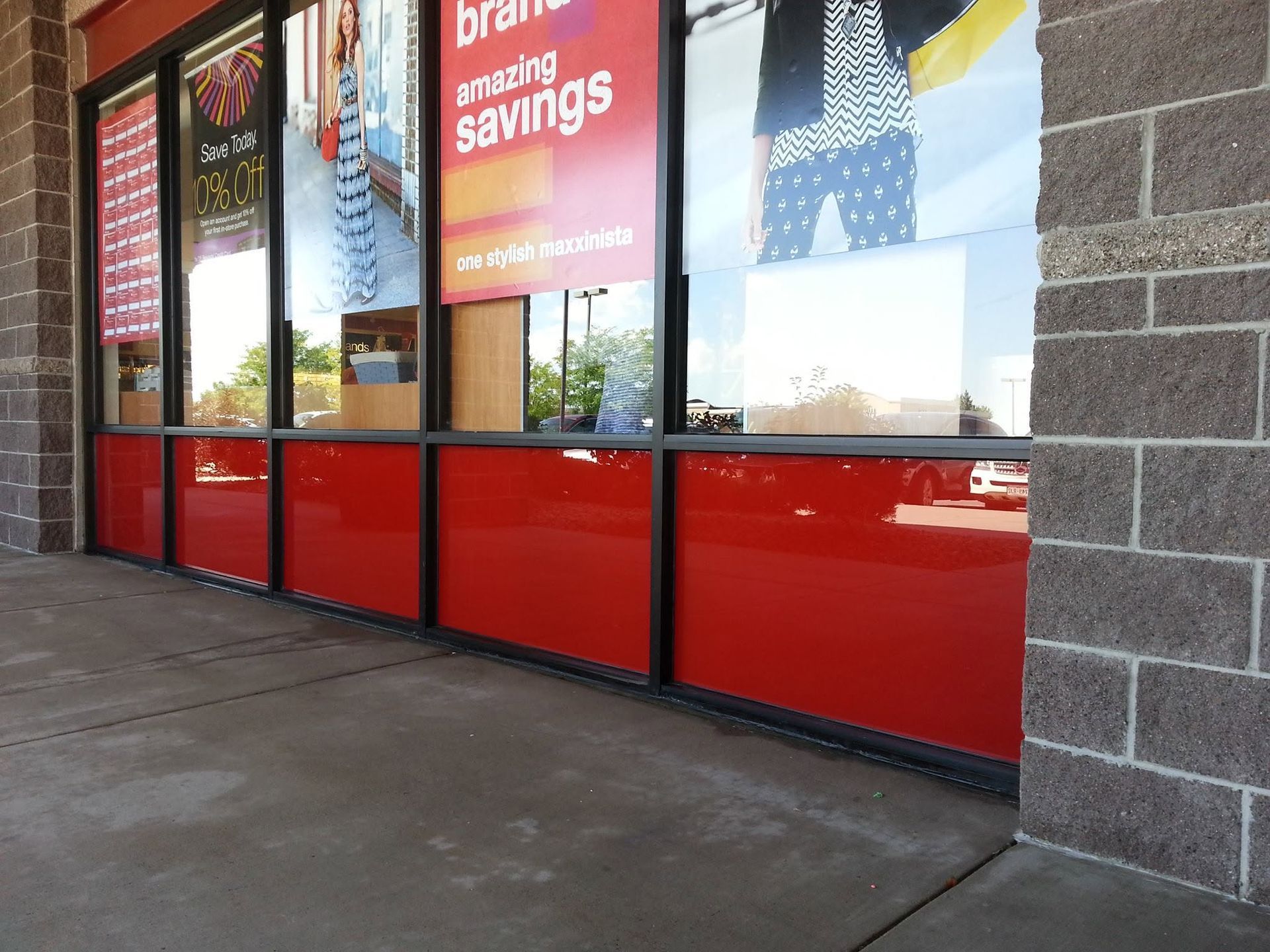 Storefront windows with red lower panels and sale signs beside a sidewalk