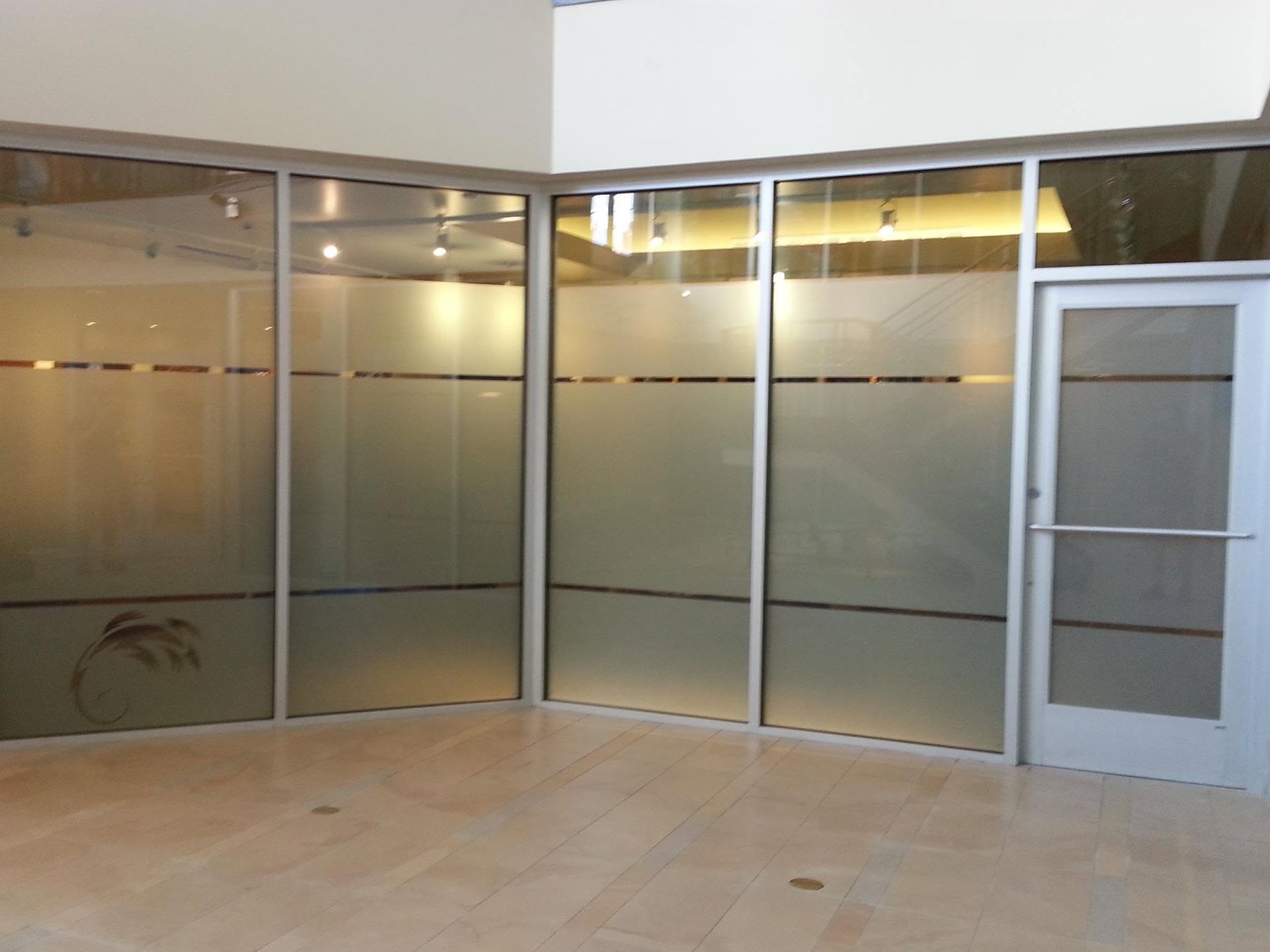 Empty storefront with frosted glass walls, tiled floor, and a white door on the right.