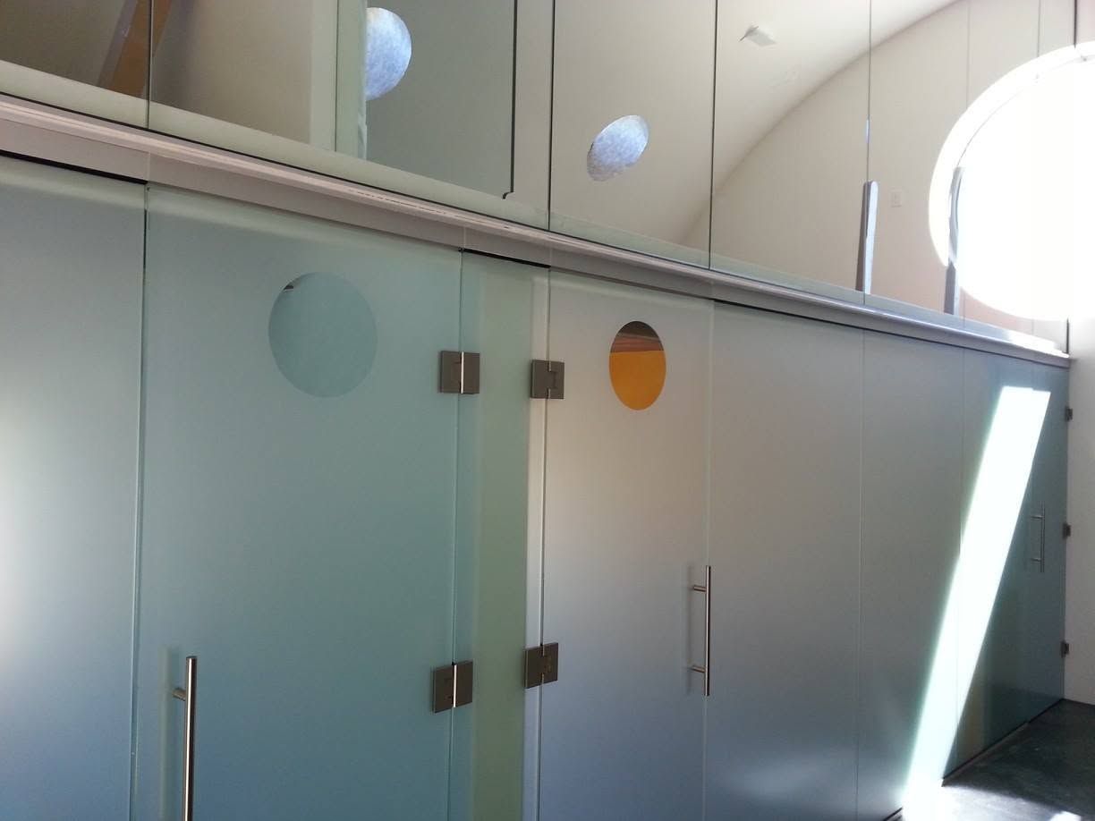 Frosted glass bathroom stall doors with metal handles in a bright public restroom