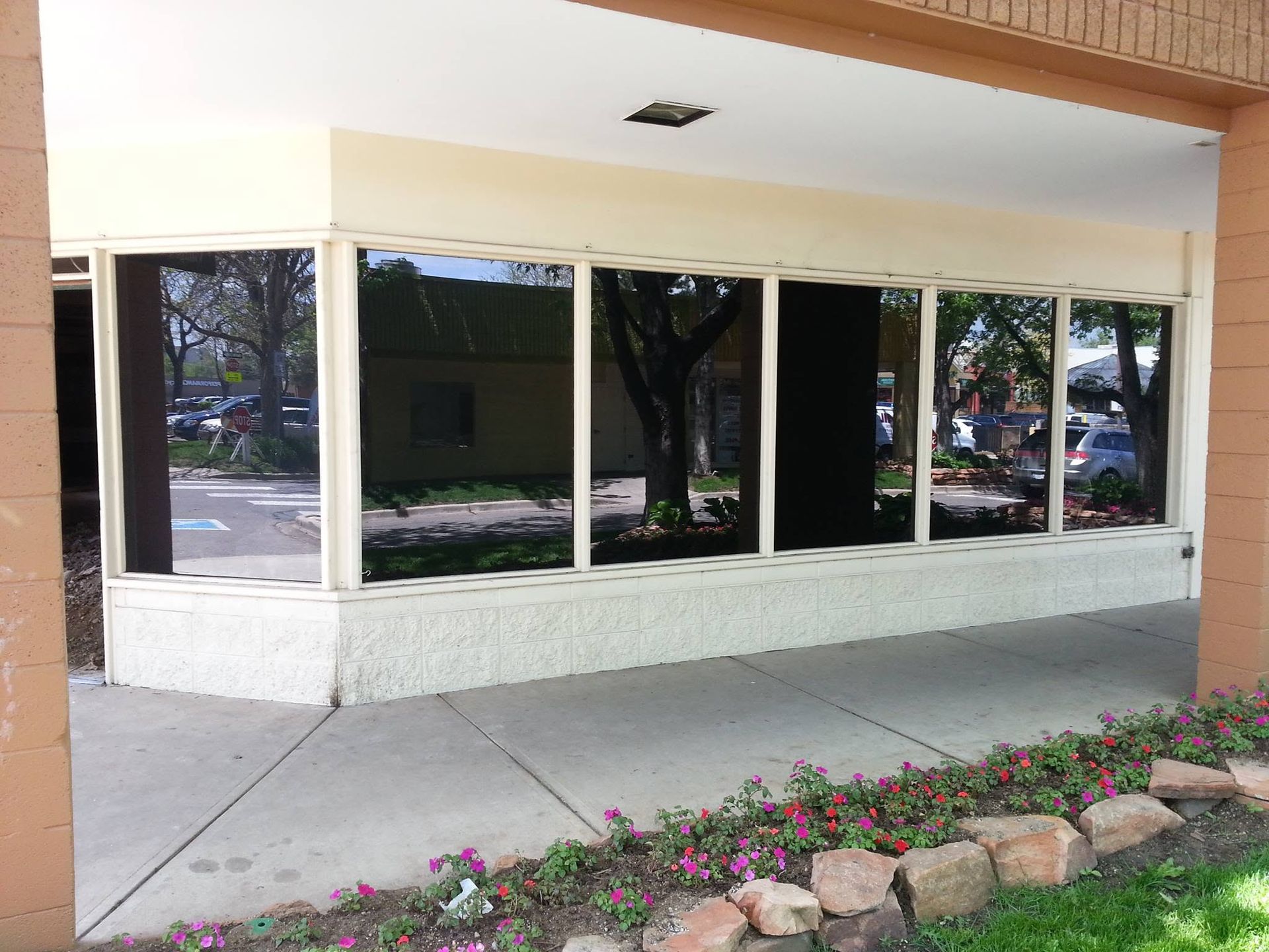 Empty storefront with large reflective windows and a flower bed along the sidewalk