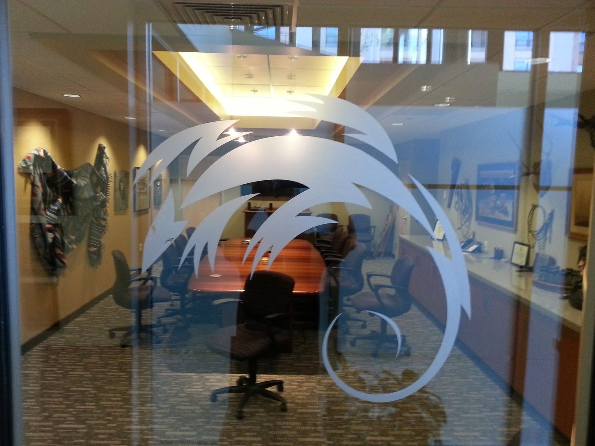 Glass-walled office conference room with swivel chairs, framed art, and large circular frosted logo on the window
