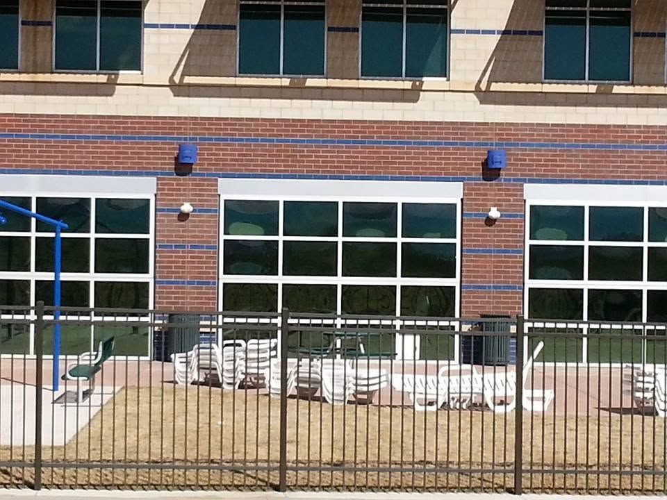 Brick building with large windows, fenced patio seating, and blue wall lights