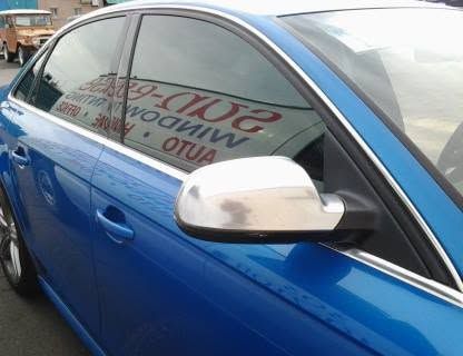 Blue car with tinted windows and a white side mirror, parked outdoors.