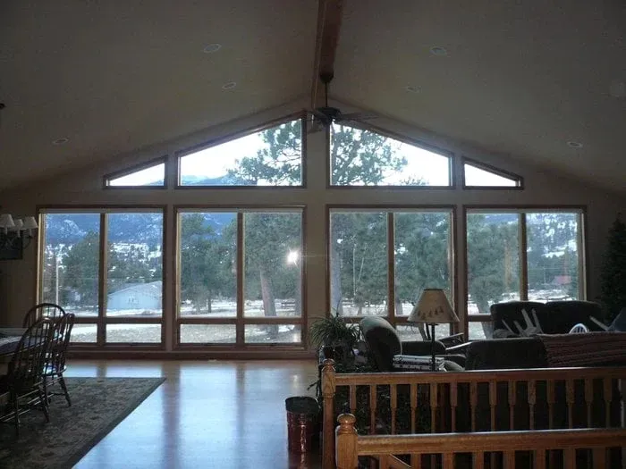 Spacious living room with large windows, high ceiling, and wooden furniture overlooking a snowy outdoor view
