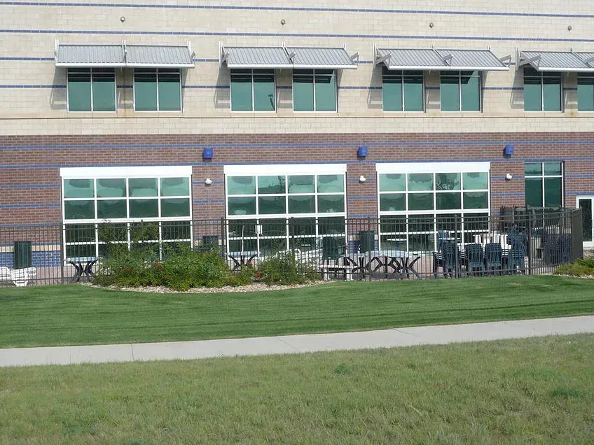 Brick school building with large windows, green awnings, and a grassy foreground