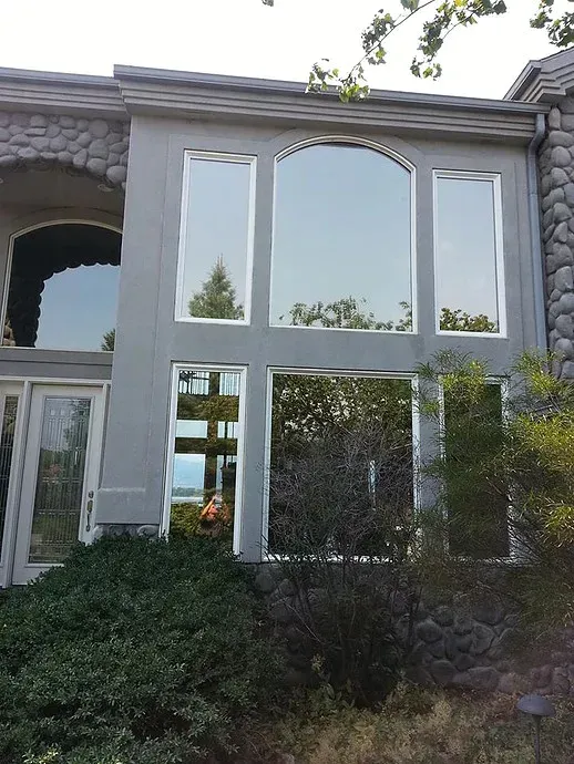 Two-story stone house facade with large arched and rectangular windows and ivy-covered landscaping